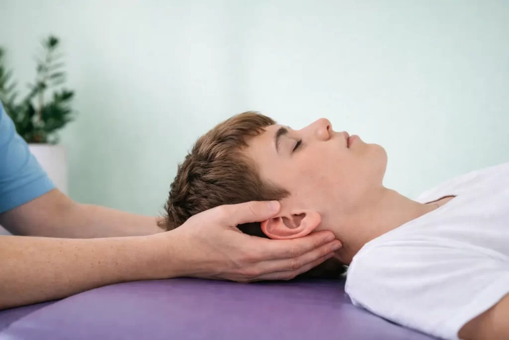 Kraniosakrální terapie v REHANEST dětské rehabilitaci Praha Barrandov – detail ženských rukou provádějících kraniosakrální terapii dospívajícímu chlapci