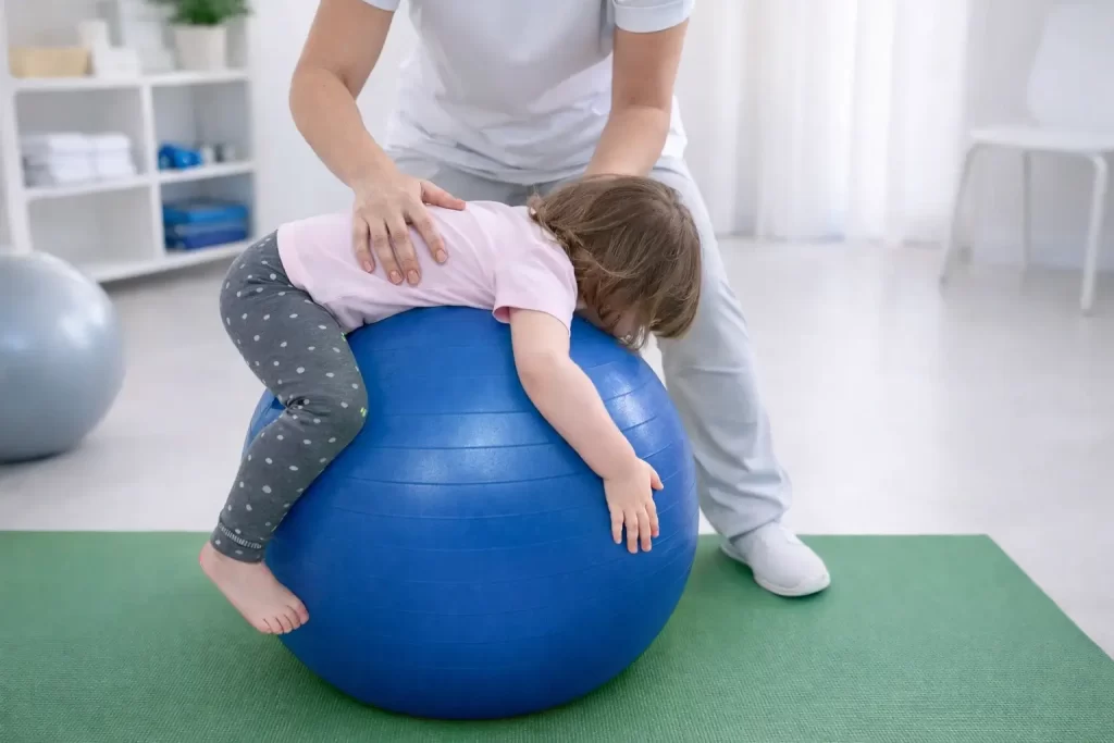 Co vás čeká v REHANEST dětské rehabilitaci Praha Barrandov – terapeutka pomáhá dítěti cvičit na rehabilitačním míči.